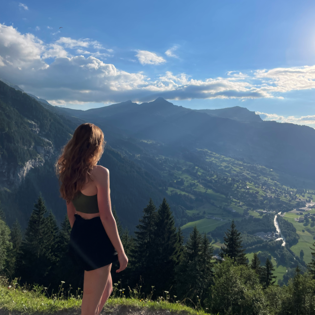 Hiking in Switzerland: Best Day Hikes in the Swiss Alps a woman hiking in switzerland overlooking views of mountains in grindelwald